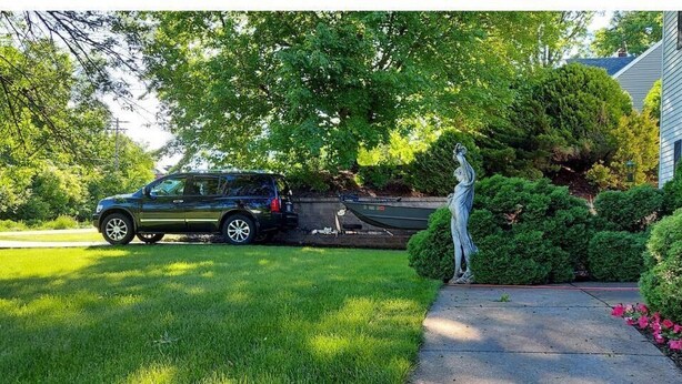 Une allée menant à une maison, avec un VUS garé, une statue et des jardins bien entretenus.