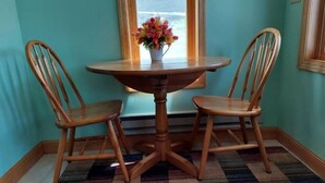 Une pièce aux murs de couleur turquoise, une table ronde en bois accompagnée de deux chaises en bois, un tapis coloré et une fenêtre ornée d’un vase de fleurs.