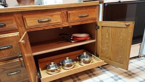 Une cuisine avec des meubles de rangement en bois, une poêle rouge posée sur une étagère et trois casseroles en métal sur une étagère inférieure.