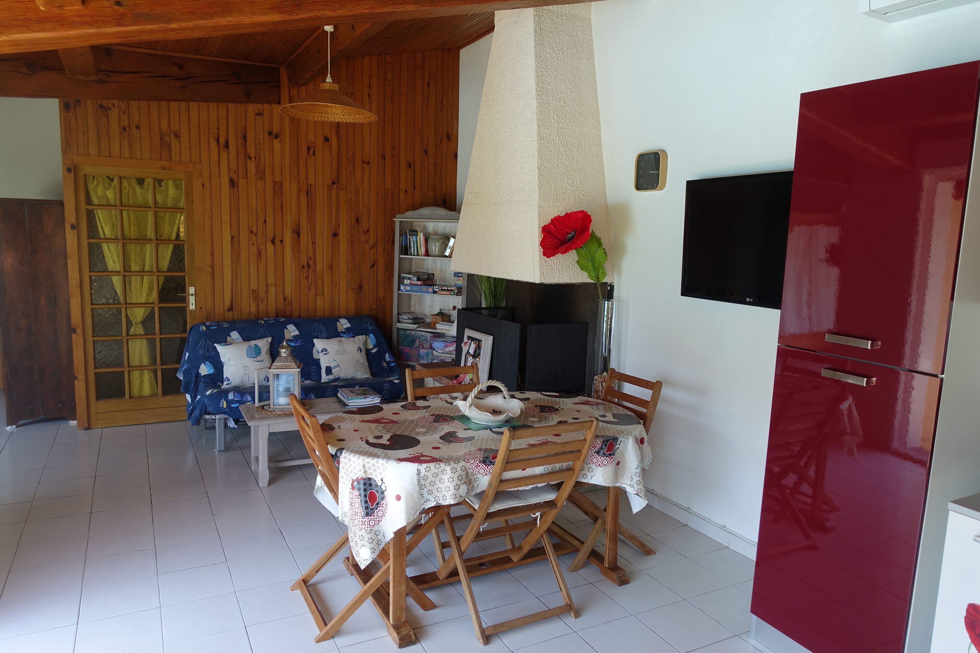 Ein Essbereich mit einem Tisch, gedeckt für vier Personen, umgeben von Holzstühlen, einem roten Kühlschrank und einem an der Wand befestigten Fernseher.