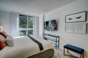 Une chambre à coucher avec un lit, une télévision, un banc et des œuvres d’art encadrées accrochées au mur.