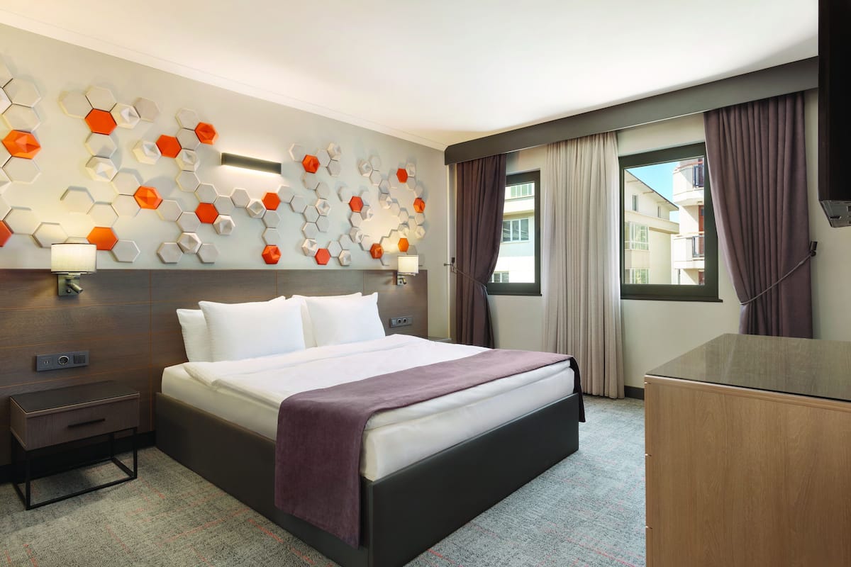 Een hotelkamer met een groot bed, een nachtkastje, een dressoir en een wand met honingraatpatroon.