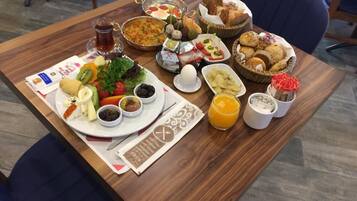 A wooden dining table with a variety of foods and drinks, including bread, fruits, and condiments.