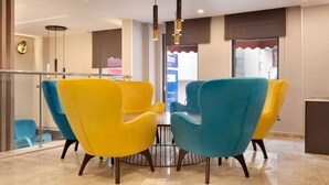 A modern dining area with a round table and four vibrant chairs, a glass railing, and a view of the reception area.