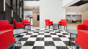 A modern indoor space with checkered flooring, red seating, and a central table.