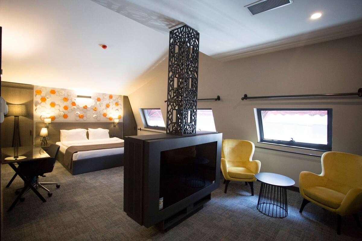 Hotelkamer met een bed, een flatscreen televisie, een bureau met stoel, twee gele fauteuils en een raam met uitzicht.