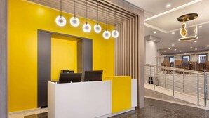 A reception desk with a modern design, a staircase, and a dining area in the background.