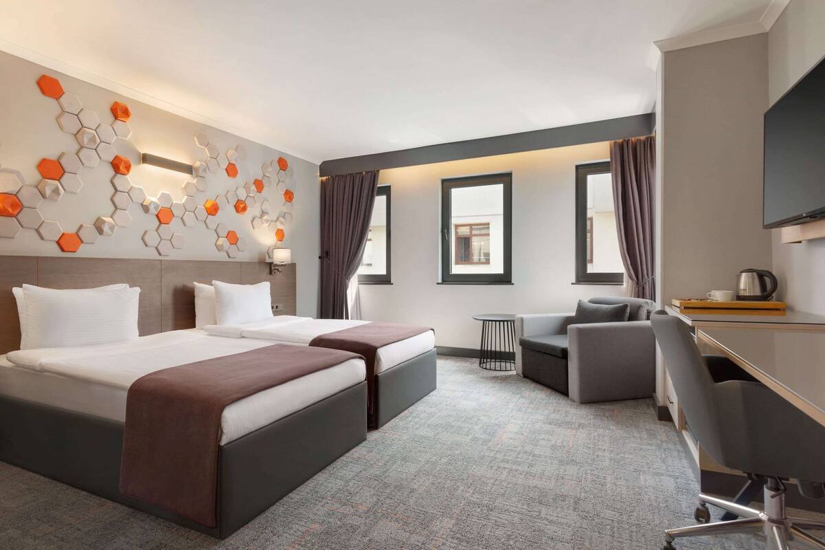 Een hotelkamer met twee bedden, een bureau, een stoel, een bijzettafeltje en een televisie.