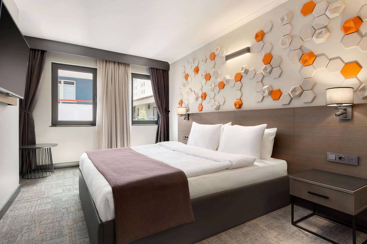 Een moderne hotelkamer met een groot bed, een nachtkastje, een wandlamp en een raam met gordijnen.