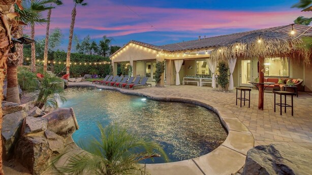 A pool area with lounge chairs and a covered seating area with string lights. - Tahiti: Walking Distance to Coachella! (Indio)