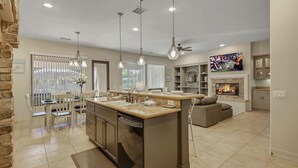 A modern kitchen with a central island, pendant lighting, and a fireplace. - Tahiti: Walking Distance to Coachella! (Indio)