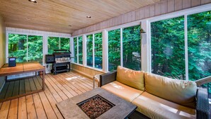 Eine Holzterrasse mit einem Steinkamin, einem Grill und einer Couch mit Kissen.