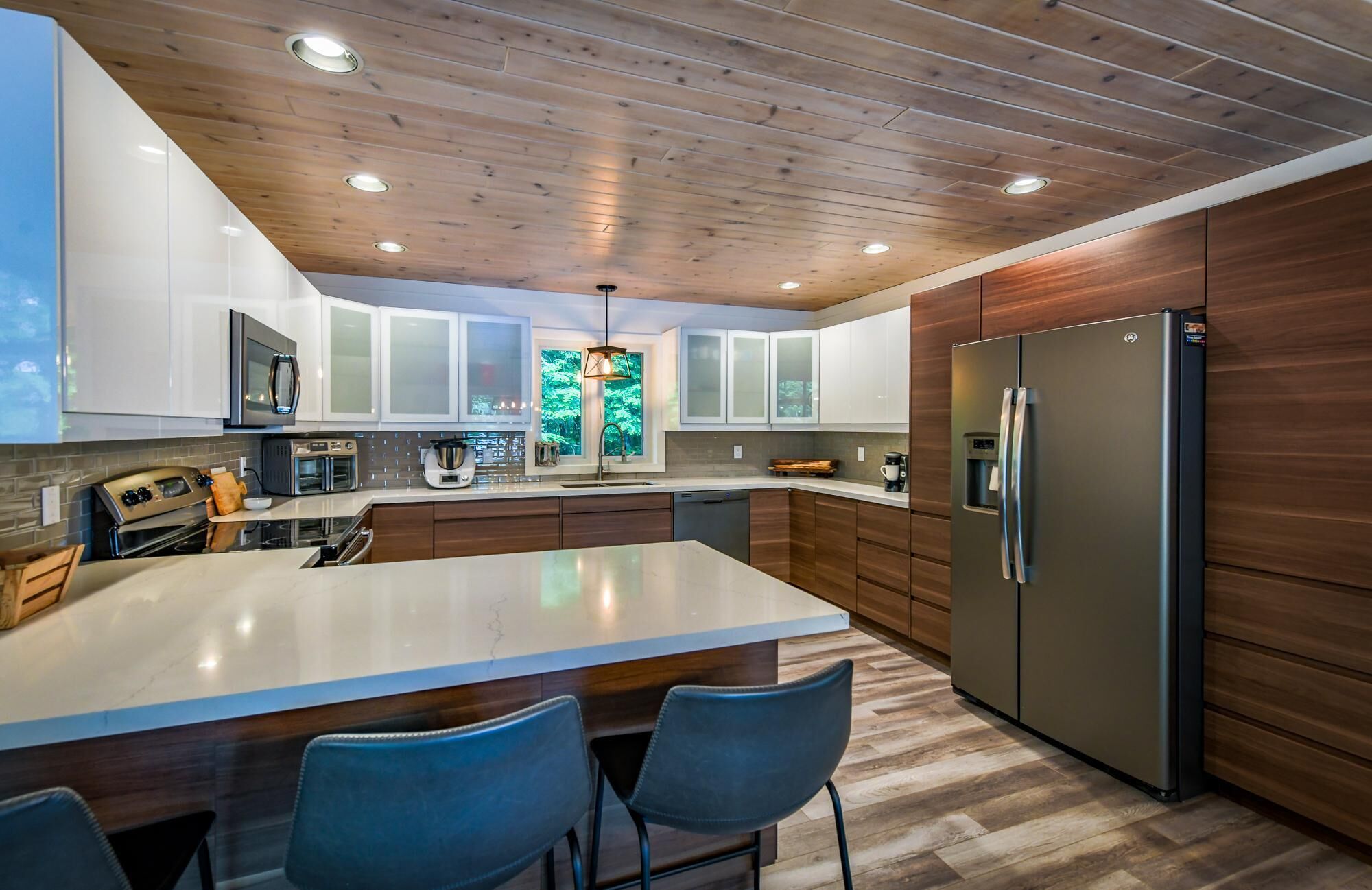 A modern kitchen with a large island, wooden cabinets, stainless steel appliances, and a built-in refrigerator.