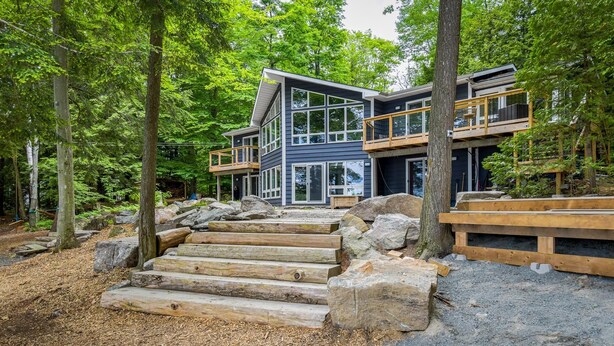 Eine moderne, zweistöckige Holzhütte mit einer Holzterrasse und einer Steintreppe, die zum Eingang führt.