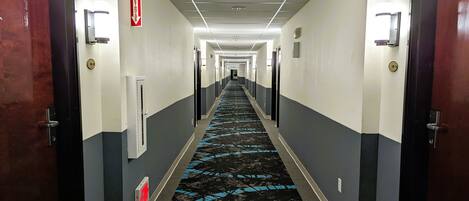 A hotel hallway with a blue carpet, doors on both sides, and a fire exit sign.
