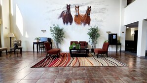 Um hall amplo com um grande mural de cavalos, uma área de estar central com uma mesa de centro e uma recepção.