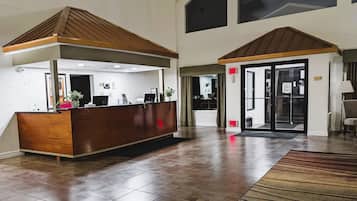 Un área de recepción con un mostrador de madera, un espacio de espera con un tapete estampado y una puerta de cristal de acceso.
