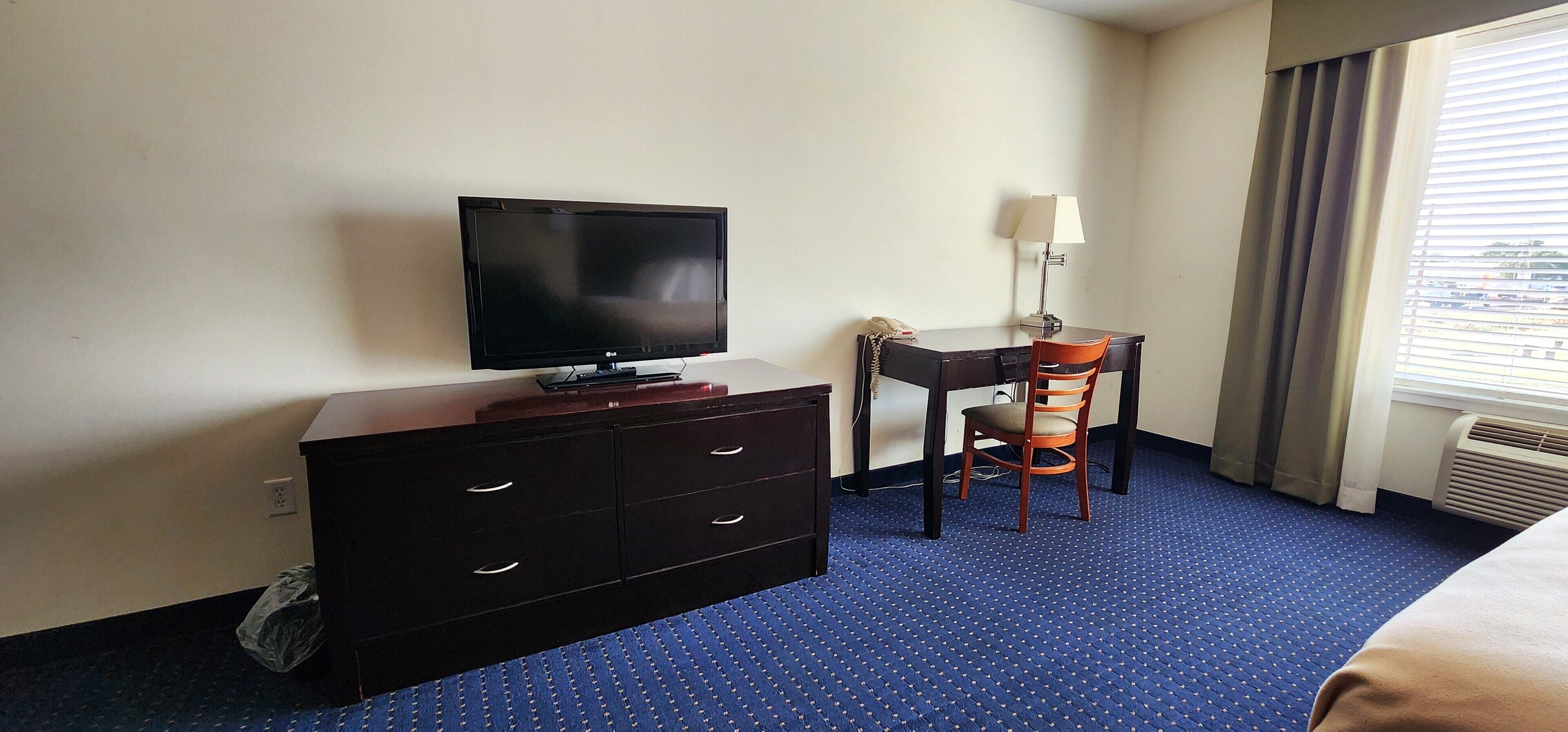 A hotel room with a flat-screen TV, a desk with a chair, a telephone, and a lamp.