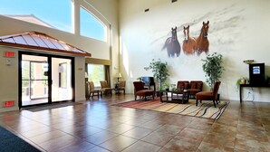Um hall amplo com um grande mural de cavalos, uma área de estar com cadeiras e uma mesa, e um sinal de saída.