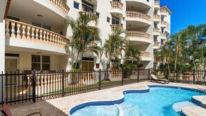 Ein Hotel mit Swimmingpool, Palmen und einer umzäunten Terrasse.