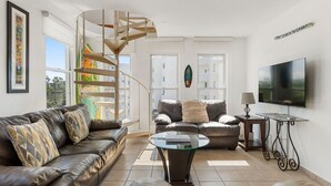 Ein modernes Wohnzimmer mit Wendeltreppe, Ledersofas, einem Glastisch und einem Flachbildfernseher.