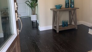 Un couloir doté d’un parquet en bois foncé, d’une porte blanche, d’une plante en pot et d’une console en bois sur laquelle sont disposés des objets en verre bleu.
