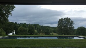 A swimming pool with a grassy area in front, surrounded by trees and a cloudy sky.