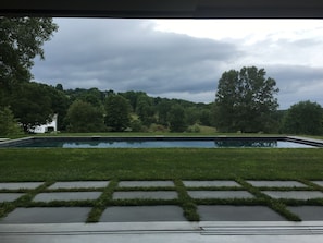 Una piscina con un área verde frente a ella, rodeada de árboles y un cielo nublado.