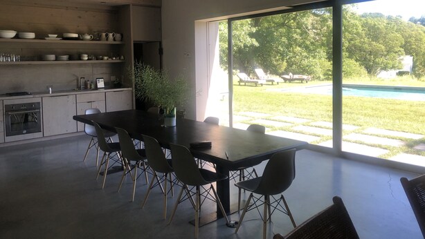 A modern kitchen with a dining area, large windows, and a view of a swimming pool.
