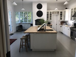 Una cocina moderna con armarios blancos, una isla central con taburetes, un amplio ventanal y un adorno circular negro en la pared.