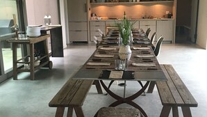 A spacious dining area with a long wooden table set for a meal, a small table with a vase of greenery, and a cozy seating area with a blanket and a small dog.