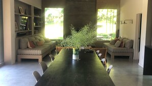 A spacious dining area with a long table, chairs, and a potted plant.