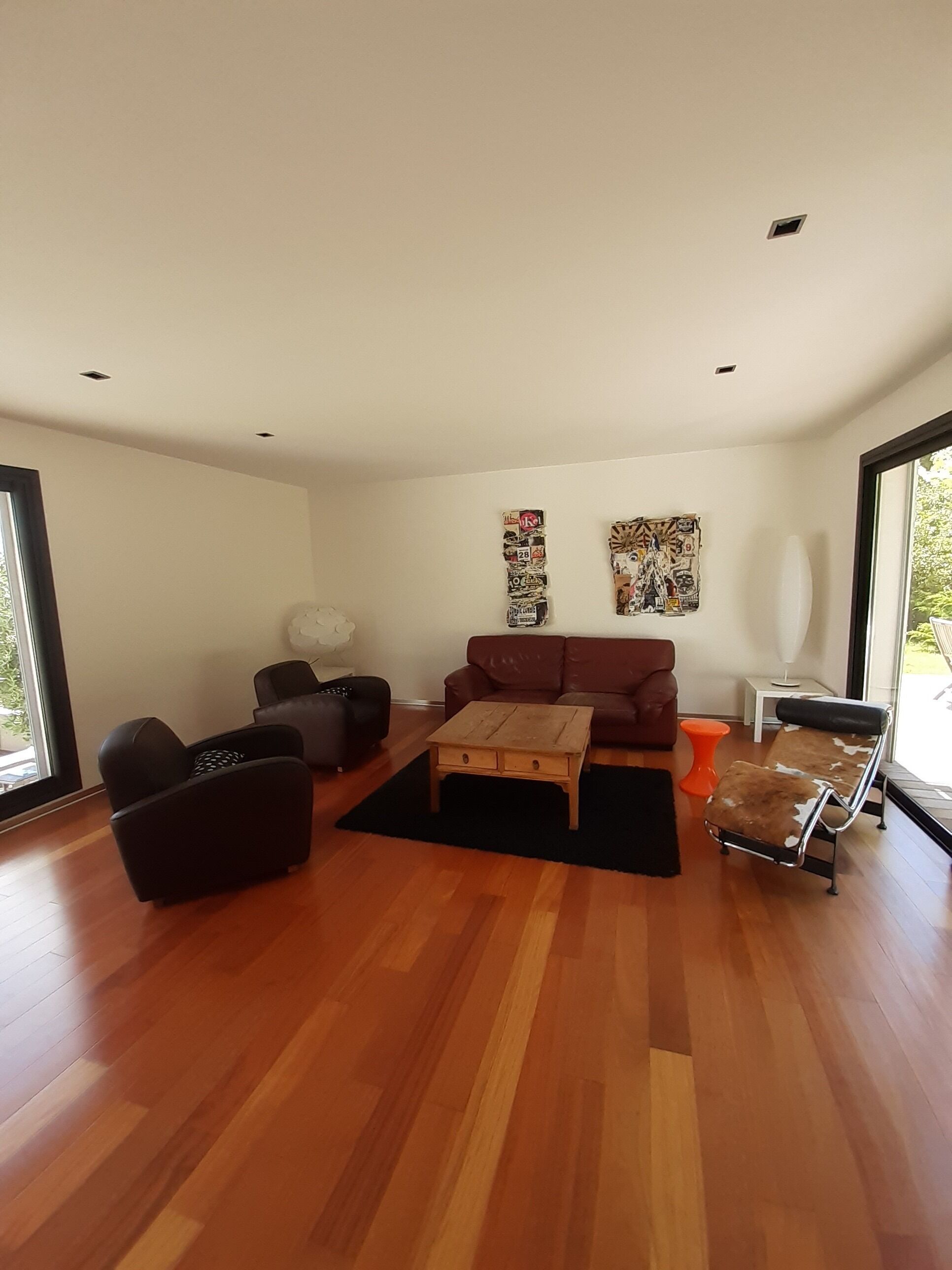 Un salon moderne avec un plancher en bois, un canapé marron, un fauteuil noir, une table basse en bois et un petit tabouret orange.
