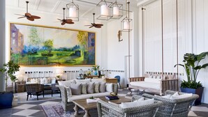 Tilava olohuone, jossa on suuri taulu, rottinkihuonekaluja, kattotuulettimia ja riippuvalaisimia.