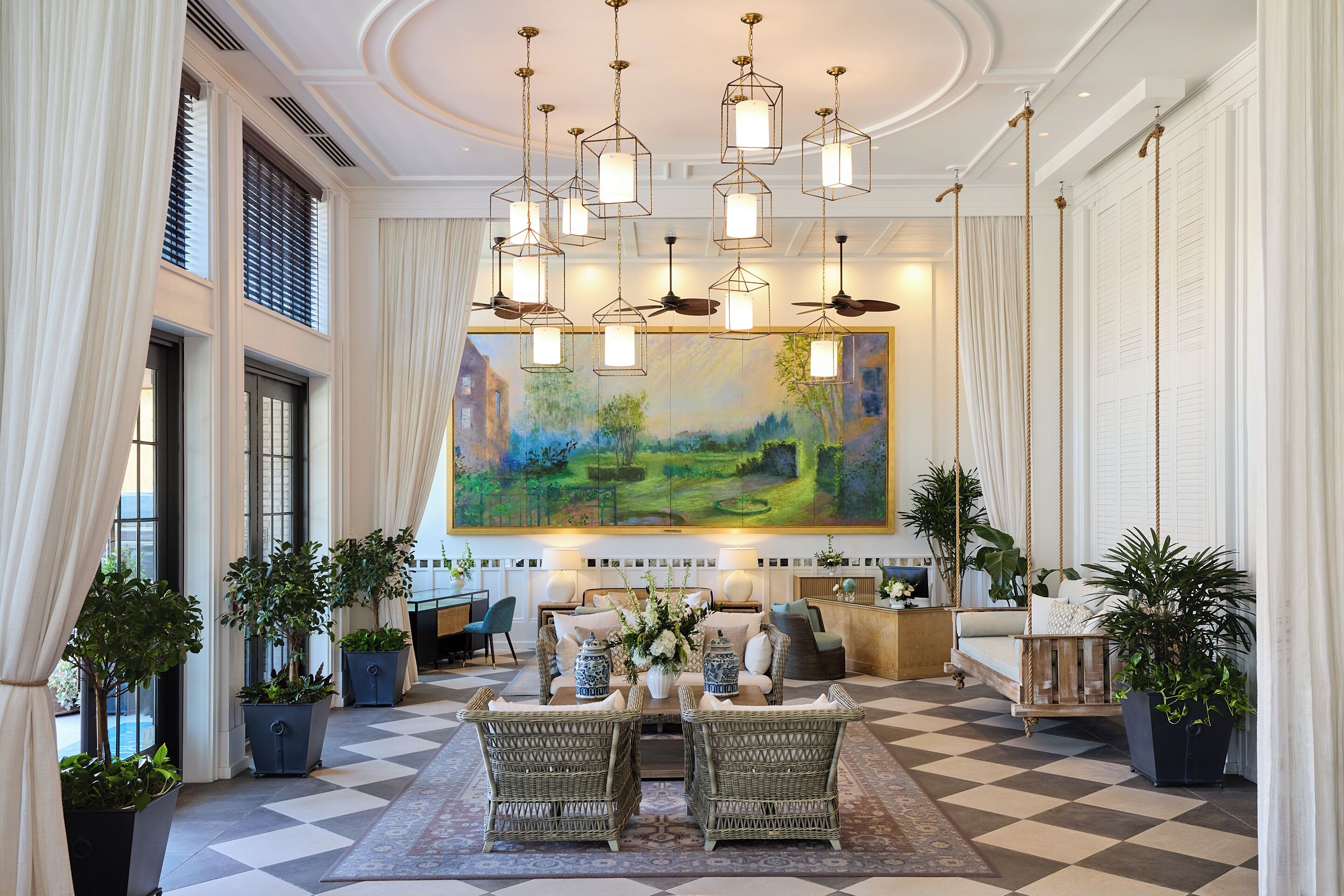 Um hall amplo com piso xadrez, uma grande pintura de paisagem e várias luminárias pendentes.