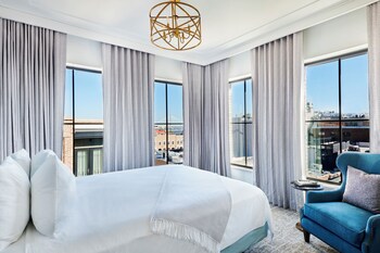 A room with two armchairs, a hexagonal table with a vase of flowers, and large windows with views of buildings and palm trees. at The Loutrel