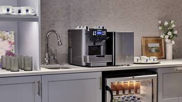 Una kitchenette con cafetera, un refrigerador lleno de bebidas y un lavamanos.