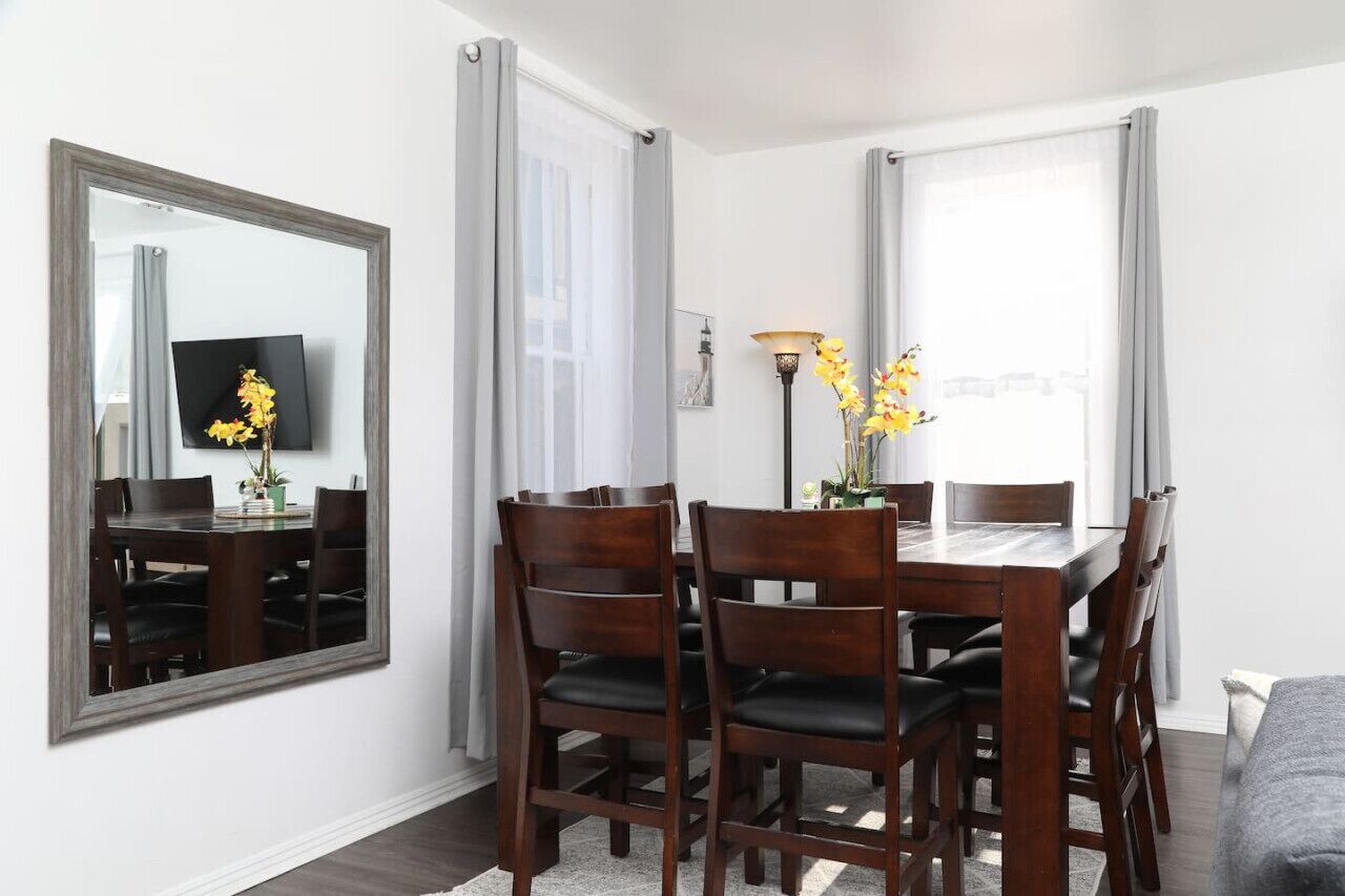 A dining area with a wooden table and chairs, a large mirror, and a vase with yellow flowers.