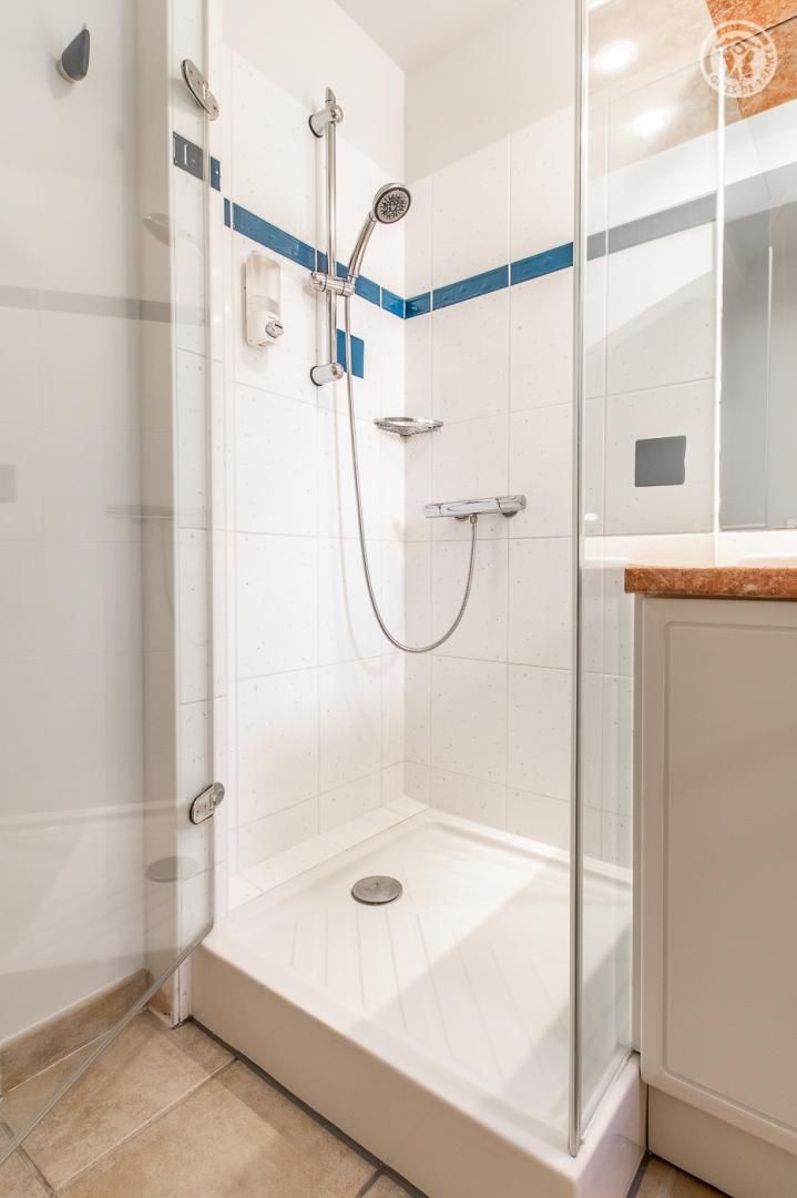 A walk-in shower with a glass door, white tiled walls, and a blue stripe.