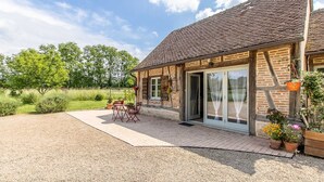 A brick house with a tiled roof, a gravel driveway, and a patio with outdoor furniture. - La Ferme de la Terve (BRUAILLES)