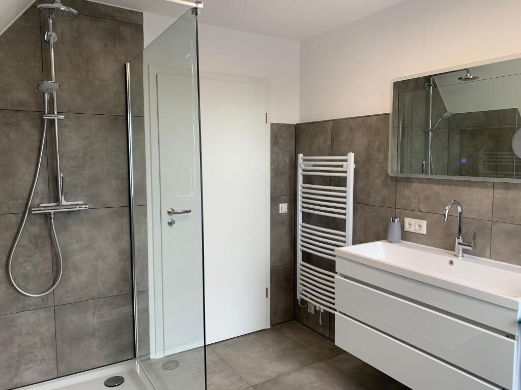 A modern bathroom with a glass-enclosed shower, a white vanity with a sink, and a towel rack.