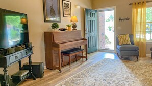 A living room with a television, a piano, a chair, and a door leading outside.