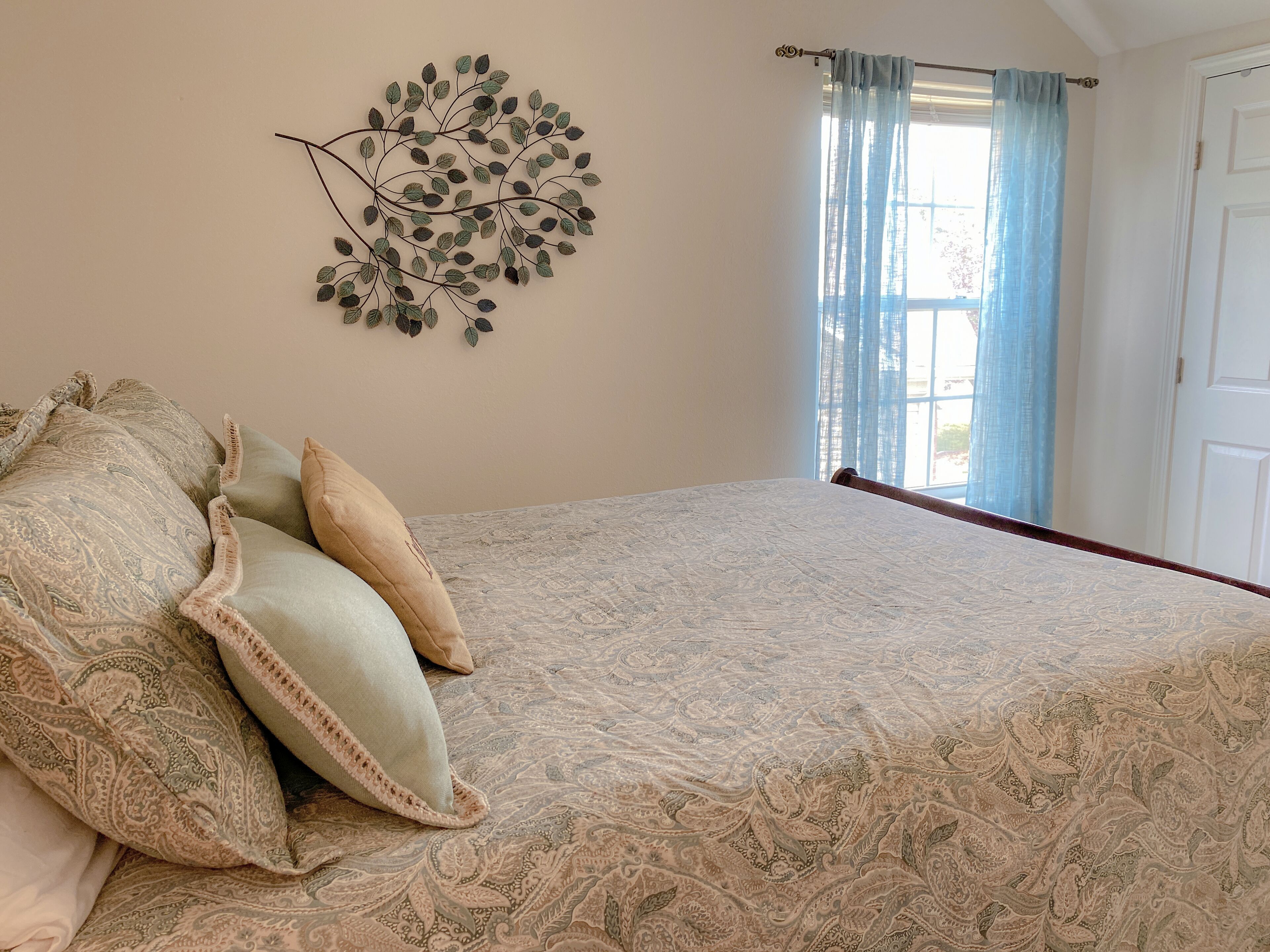 A bedroom with a bed, patterned bedspread, decorative wall art, and a window with curtains.