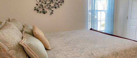 A bedroom with a bed, patterned bedspread, decorative wall art, and a window with curtains.