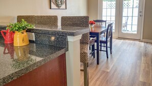A kitchen with granite countertops, a dining area with a wooden table and chairs, and a view through a glass door.
