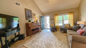 A living room with a television, a piano, a sofa, and a patterned rug.