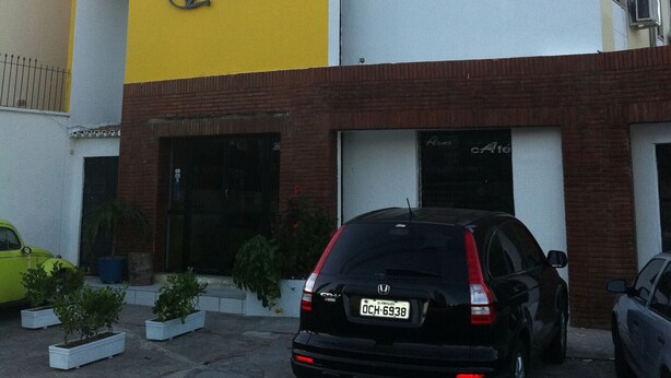 Un hôtel à la façade jaune et blanche, avec une voiture noire garée devant et des plantes en pot près de l’entrée.