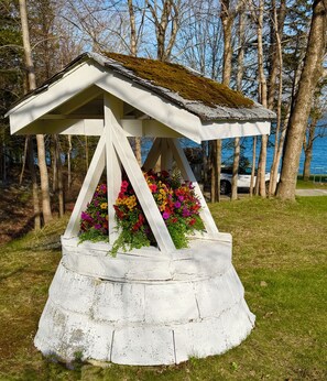 A gazebo with a moss-covered roof and a flower bed in front.