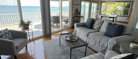 A spacious living room with a large sofa set, a coffee table, and a view of the ocean through large sliding glass doors.