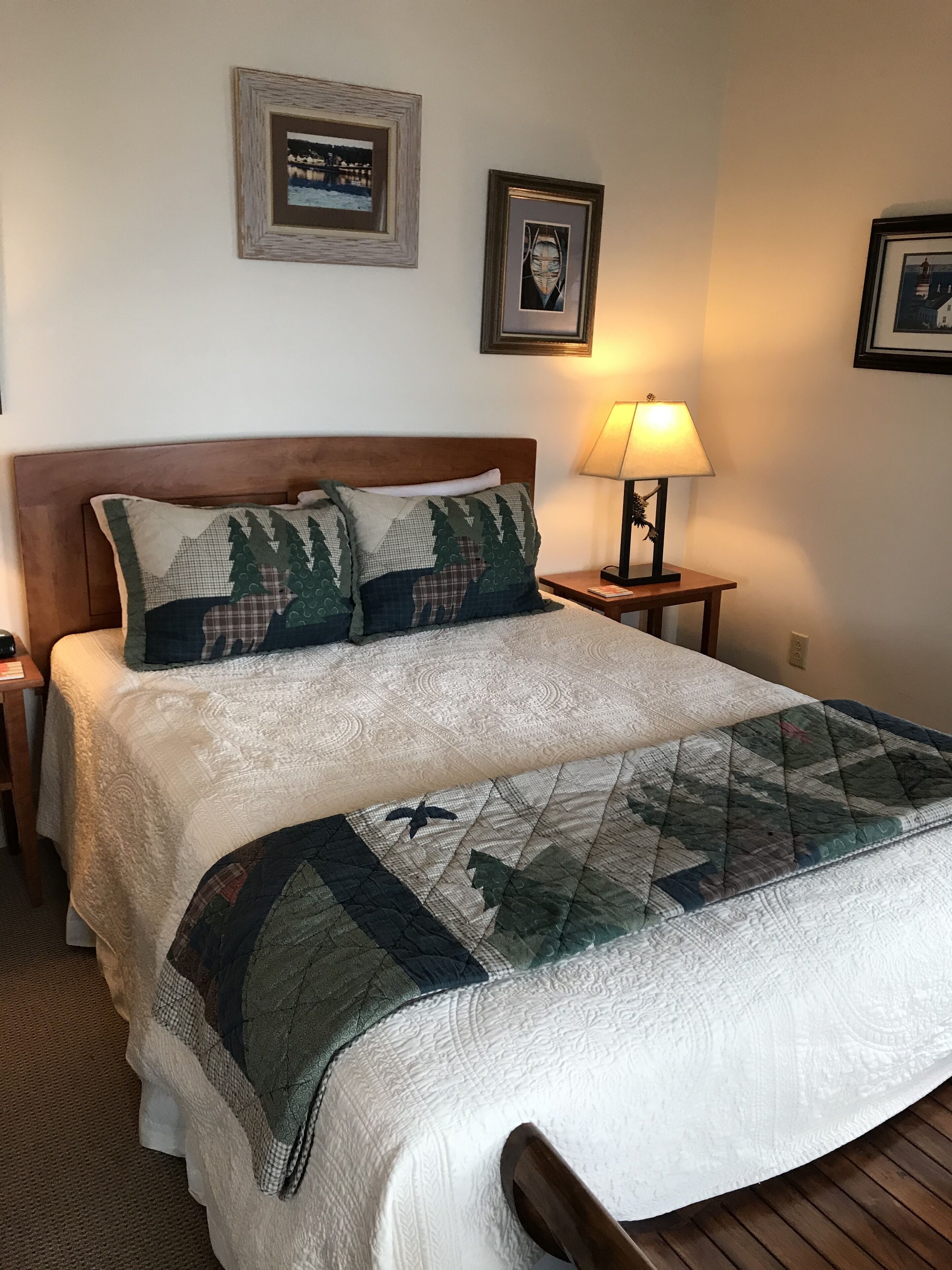 A neatly made bed with a quilt, a wooden headboard, and two framed pictures on the wall.
